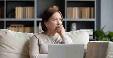 En eftertänksam kvinna sitter i en soffan med en dator i knät