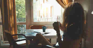En kvinna sitter vid ett bord och dricker ur en kopp