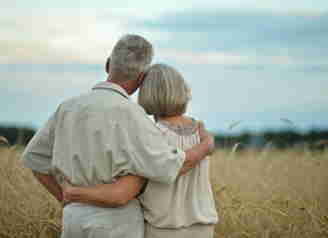 Ett äldre par som håller om varandra och ser ut över ett fält
