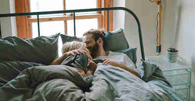 En kvinna och en man ligger i en säng och kramar varandra