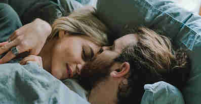 En kvinna och en man ligger i en säng och omfamnar varandra