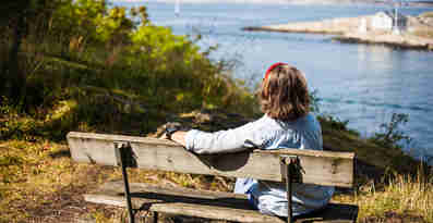 En kvinna sitter på en bänk och blickar ut över havet