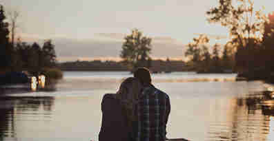En kvinna och en man sitter nära intill varandra på en brygga och blickar ut över vattnet. 