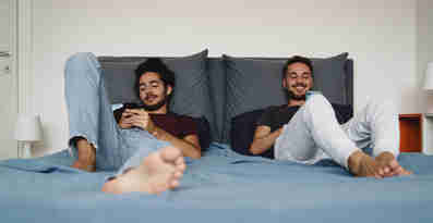 Två män ligger i sängen och kollar på sina mobiltelefoner