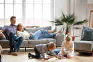 En man och en kvinna sitter i sin soffan medan deras barn leker på golvet