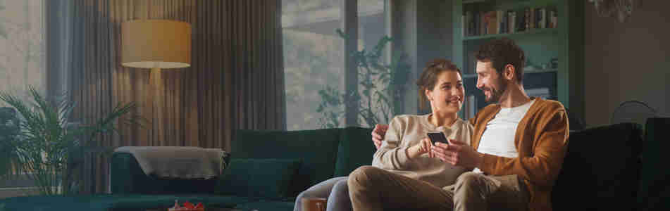 Par som sitter i soffa och tittar på en mobil tillsammans